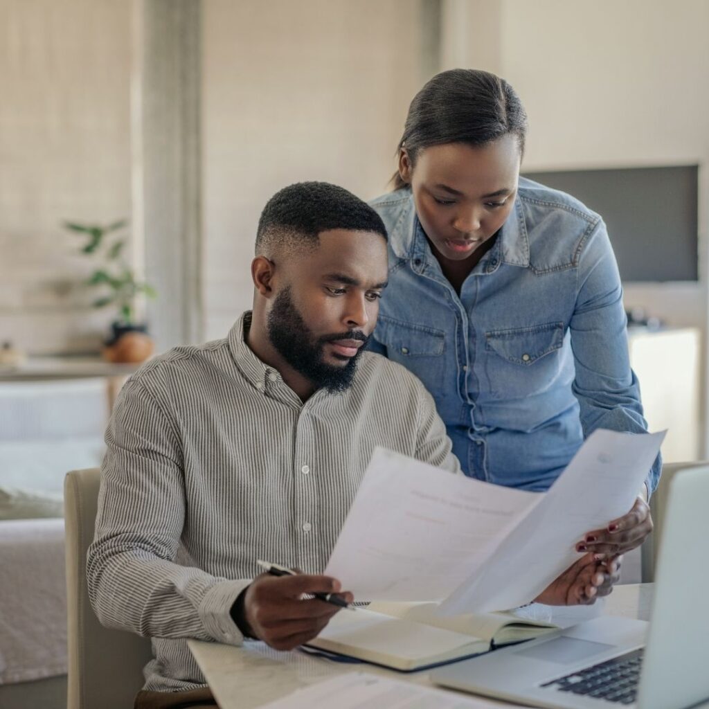 A concerned couple sitting together at a desk reviewing financial documents and monthly utility bills.