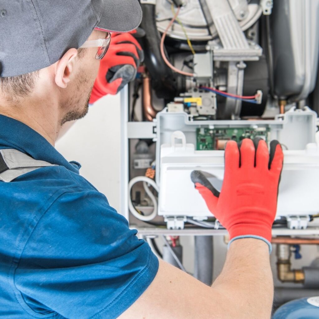 An HVAC technician wearing protective gloves repairs internal electrical components on an HVAC system.